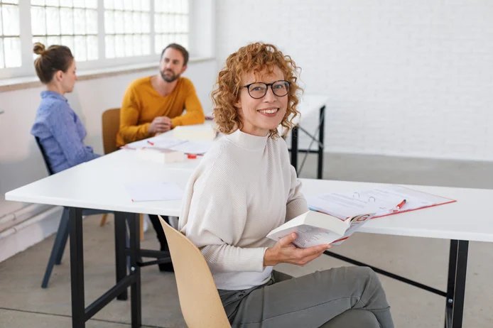Frau sitzt am Tisch mit Buch in der Hand