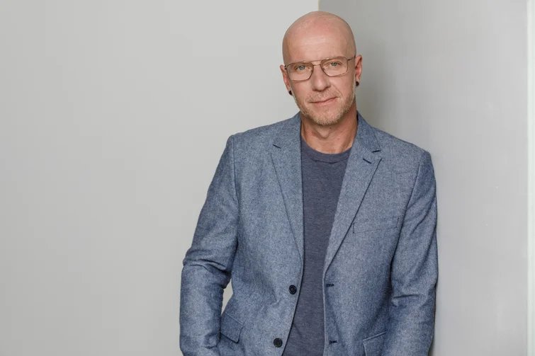 Ein Mann mit Anzug steht vor einer grauen Wand