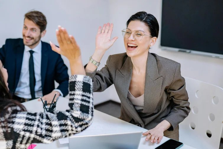 Zwei Frauen geben sich im Büro ein High Five, während ein Kollege im Hintergrund lächelt – das Bild steht für erfolgreiche Zusammenarbeit und gelebte Inklusion im Arbeitsumfeld.
