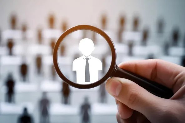 Lupe fokussiert eine Personensilhouette vor einer Gruppe – Symbol für die Neuwahl des Betriebsrats.