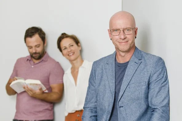 Ein Mann steht im Vordergrund und im Hintergrund befinden zwei Kollegen