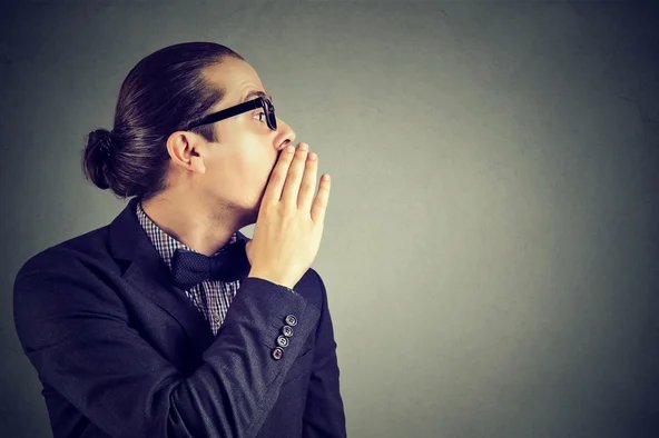 Ein Mann hält sich die Hand vor den Mund und flüstert das Hinweisgeberschutzgesetz